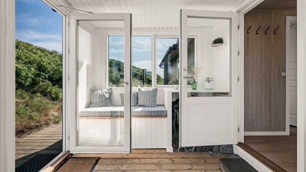 Un espacio habitable moderno y abierto con terraza de madera, área de descanso integrada y vistas del paisaje circundante.