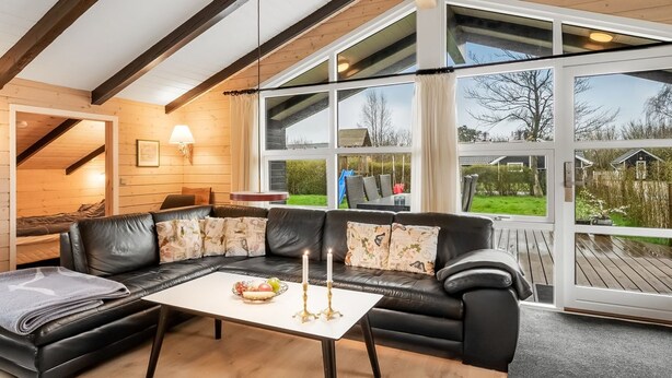 Una sala de estar moderna con un sofá seccional de cuero negro, una mesa de centro blanca con velas, y ventanas amplias con vistas al exterior.
