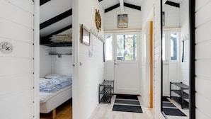 Un pasillo estrecho con una cama, un radiador y una puerta que da a otra habitación.