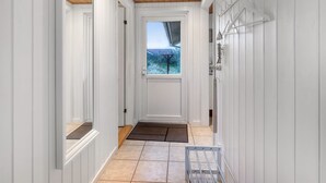 Un couloir aux murs blancs, avec un plafond en bois, une fenêtre donnant sur un paysage et un présentoir en métal.