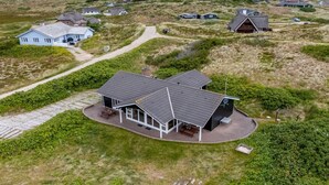 Une maison moderne dotée d’une grande terrasse, entourée d’un paysage naturel.