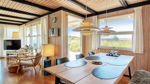 A spacious room with a wooden floor, a dining table with chairs, a TV, and a large window with a view of the outdoors.