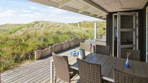An outdoor patio with wicker furniture and a table set for two, overlooking a dune landscape.