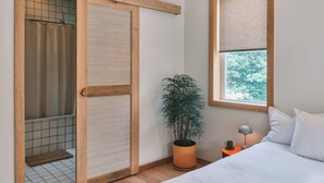 A bedroom with a bed, a window with a view, a potted plant, and a nightstand with a lamp. - guesthouse by good neighbor (Baltimore)