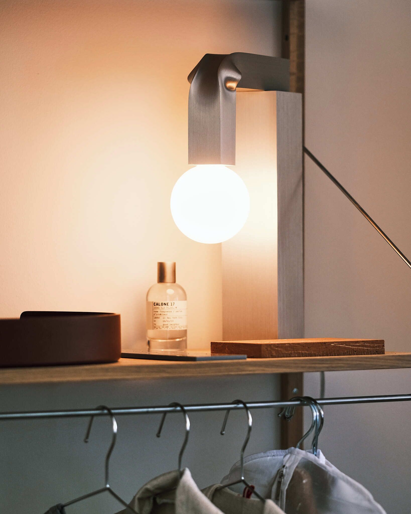 A modern bathroom with a minimalist design, featuring a round mirror, a sleek light fixture, and a bottle of Calone 17 on a shelf.