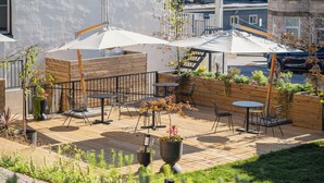 An outdoor patio area with wooden flooring, metal chairs, tables, and umbrellas. - guesthouse by good neighbor (Baltimore)