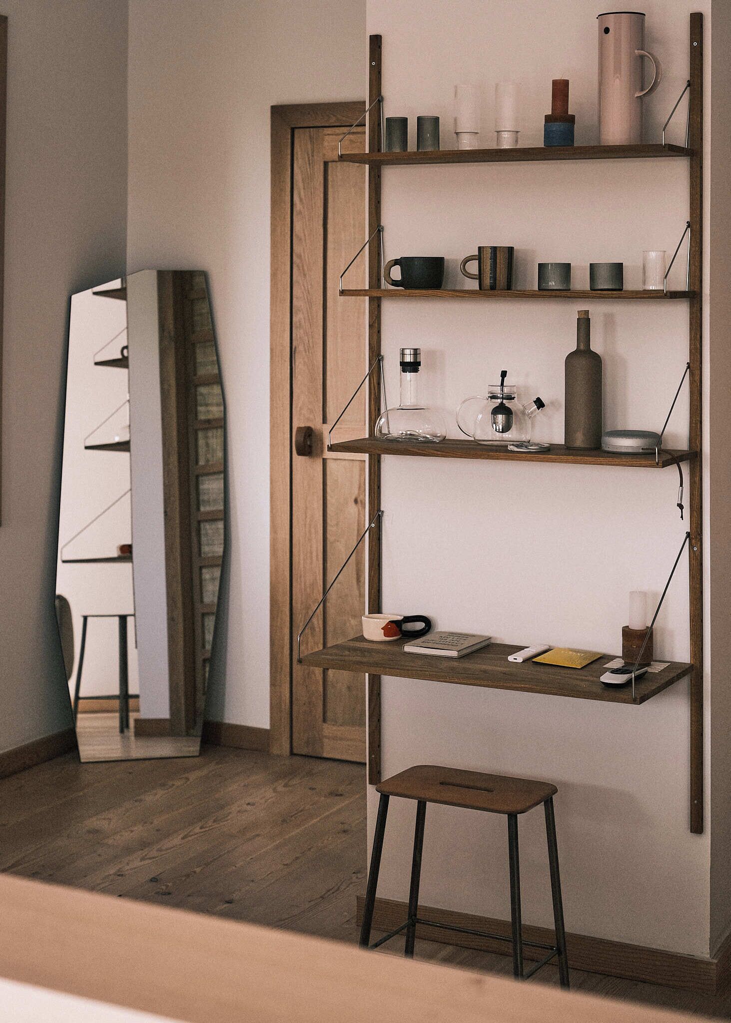 A room with a wooden floor, a white chair, a wooden bookshelf with various items, and a small stool.
