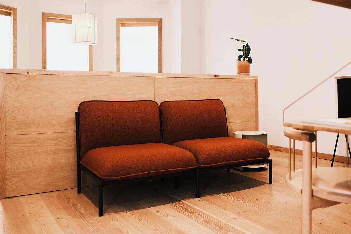 A modern room with a wooden partition, two cushioned seating areas, a small round table, and a potted plant.
