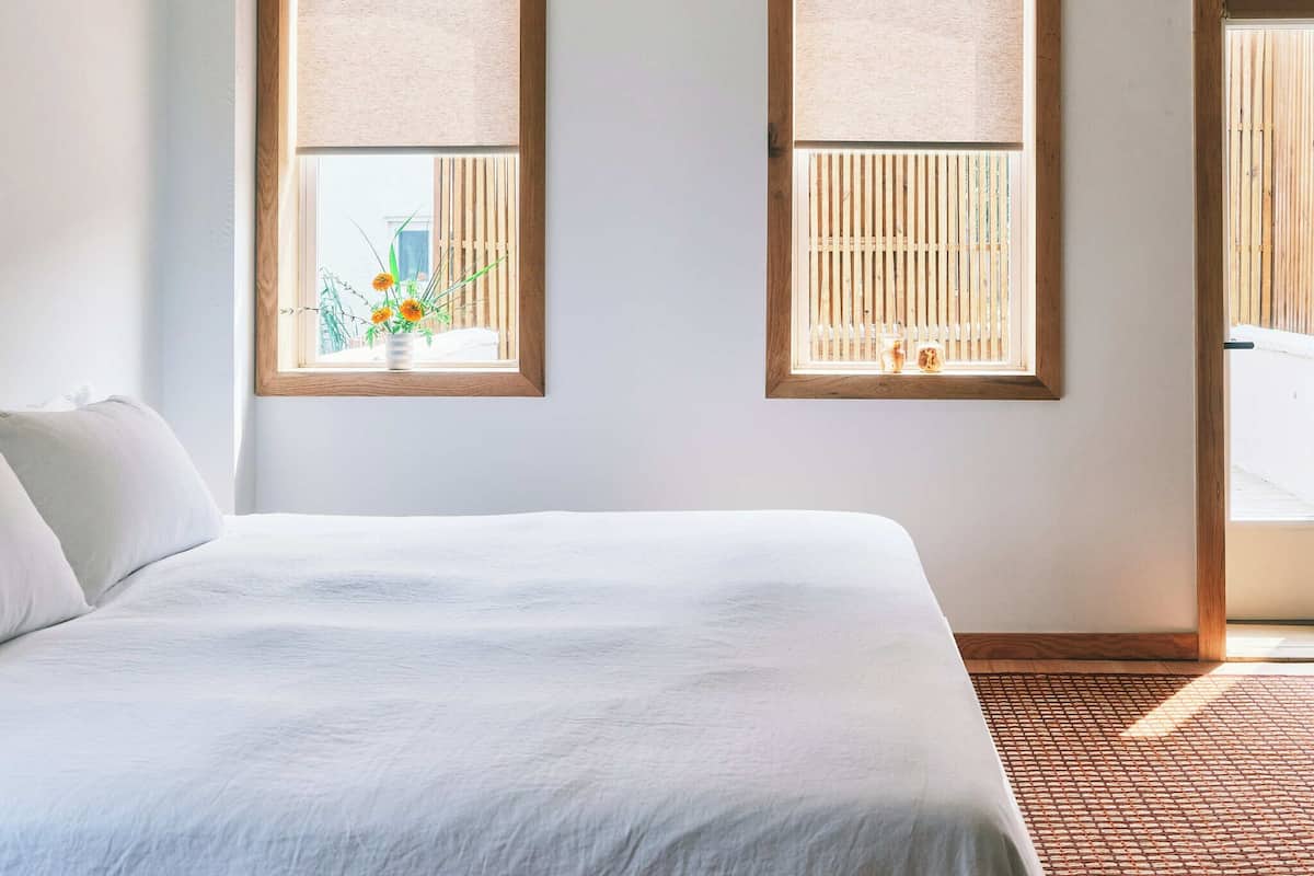 A bedroom with a large bed, two windows with wooden blinds, and a view of a balcony.