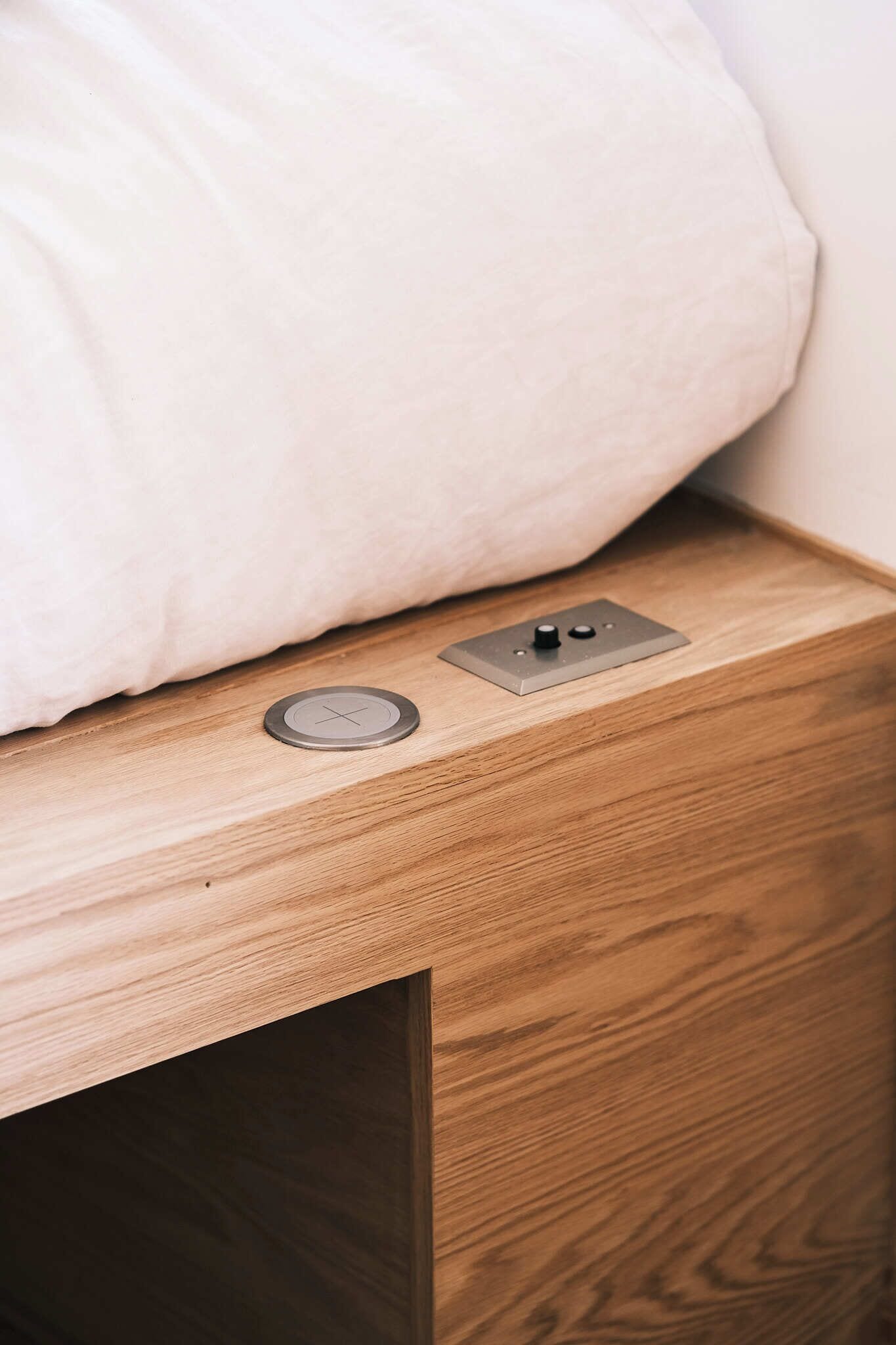 A wooden bedside table with a white pillow and a small, round, metallic object on it.