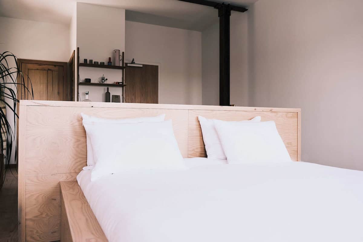 A neatly made bed with a wooden headboard and white bedding in a modern room with a wooden cabinet and shelves.