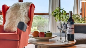 Um espaço de estar acolhedor com vista para o exterior, uma garrafa de vinho e um prato de frutas.