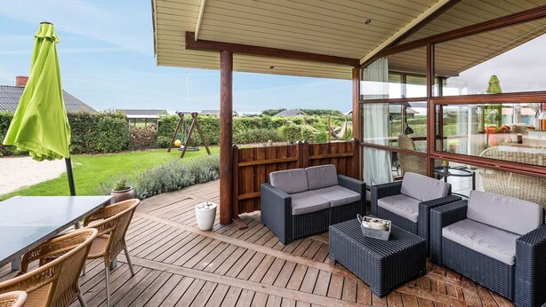 Uma área de varanda coberta com móveis de vime, uma mesa e um guarda-sol verde.