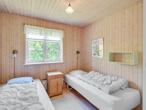 Une pièce aux murs en bois, avec deux lits, une petite armoire, une fenêtre donnant sur un beau paysage et un luminaire.