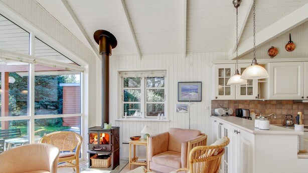 A cozy room with a large window, a fireplace, wicker furniture, and a kitchen area. - "Nela" - 300m from the sea by Interhome (Grenaa)