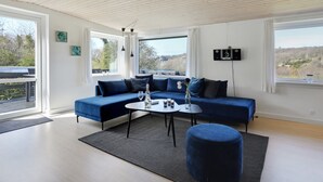 Ein modernes Wohnzimmer mit einem blauen Sofa, einem runden Couchtisch und Blick ins Freie durch große Fenster.