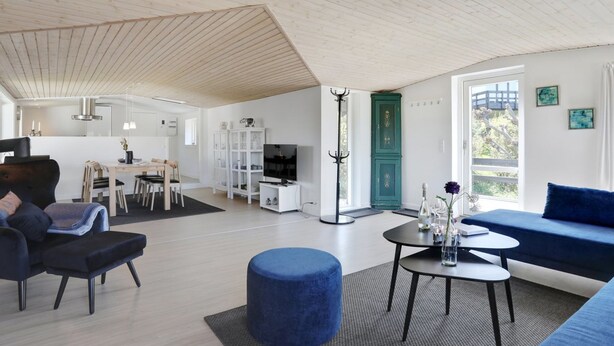 Ein modernes Wohnzimmer mit Essbereich, einem blauen Hocker und einem türkisgrünen Schrank.
