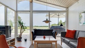 Ein geräumiger Wohnbereich mit großem Fenster, Holzboden und Blick ins Freie.