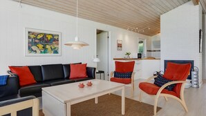 Ein modernes Wohnzimmer mit einer Couch, Sesseln, einem Couchtisch und einer Küche im Hintergrund.