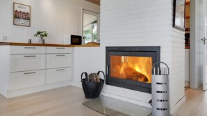 Eine moderne Küche mit weißen Schränken, einer eingebauten Mikrowelle, einem Kamin mit Holzscheiten und einem schwarzen Wasserkocher auf dem Herd.