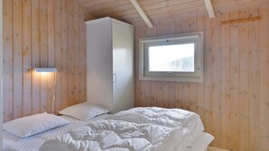 A bedroom with wooden walls, a bed with white bedding, a wardrobe, and a window with a view. - "Styrbiorn" - 100m from the sea by Interhome (Løkken)
