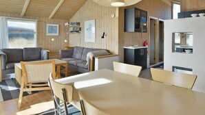 A cozy, well-lit cabin interior with a dining area, two sofas, a kitchen, and a large window. - "Styrbiorn" - 100m from the sea by Interhome (Løkken)