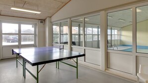 A room with a ping pong table, large windows, and a view of a swimming pool. - "Soufiane" - 100m from the sea by Interhome (Vejers Strand)