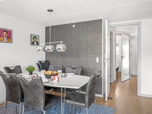 A modern dining area with a white table, grey upholstered chairs, and a grey textured wall.