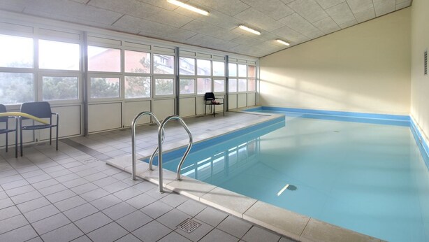 An indoor swimming pool with clear glass walls, a tiled floor, and a metal ladder. - "Soufiane" - 100m from the sea by Interhome (Vejers Strand)