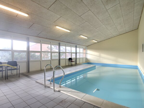 An indoor swimming pool with clear glass walls, a tiled floor, and a metal ladder.
