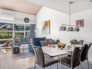 Un comedor moderno con una mesa blanca, sillas grises tapizadas y un amplio ventanal con vistas a un jardín.