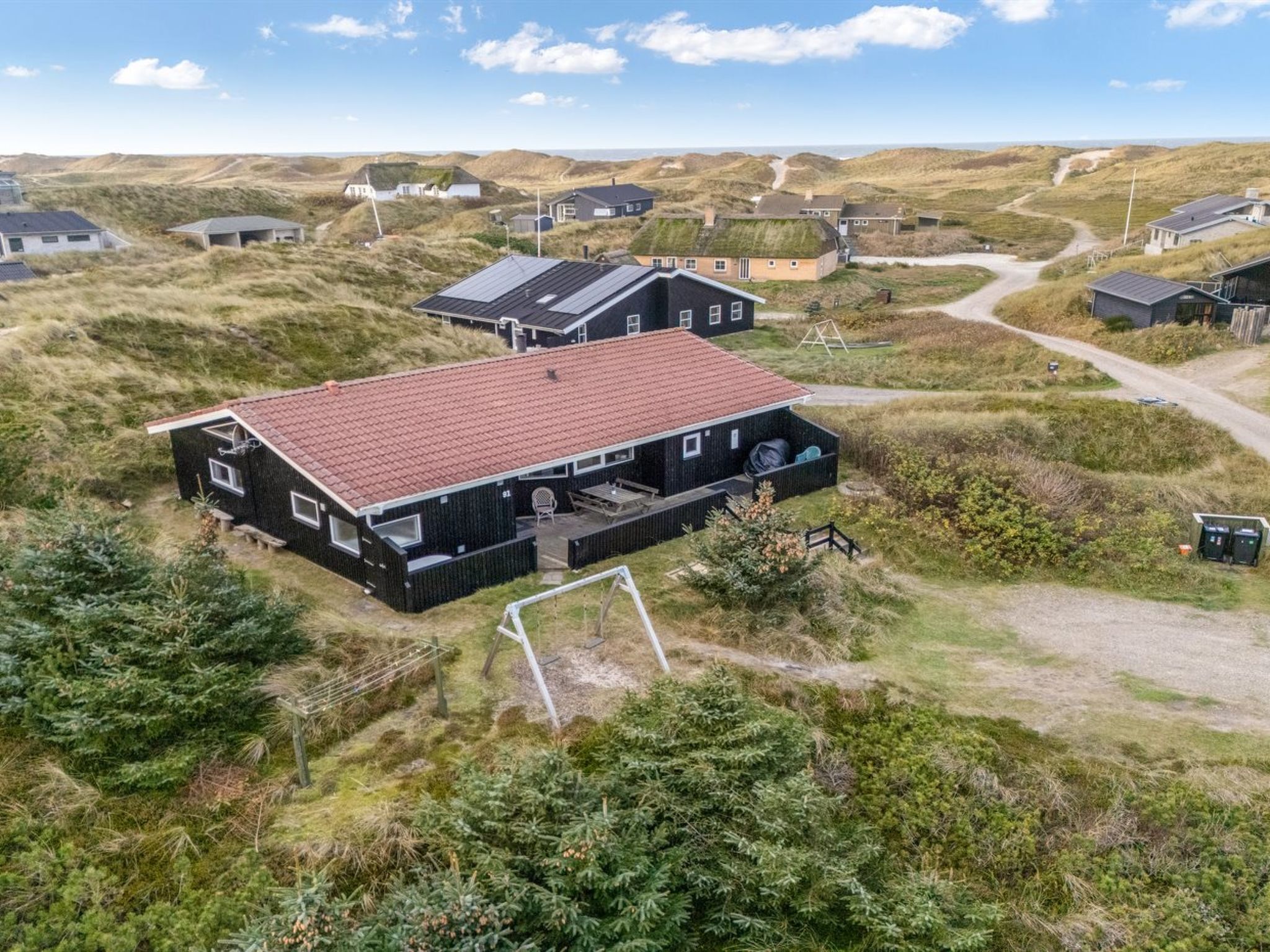 A modern house with a red roof, surrounded by a natural landscape.