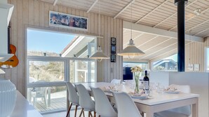 Et moderne spiseområde med et hvidt bord, grå stole og hængende lamper.