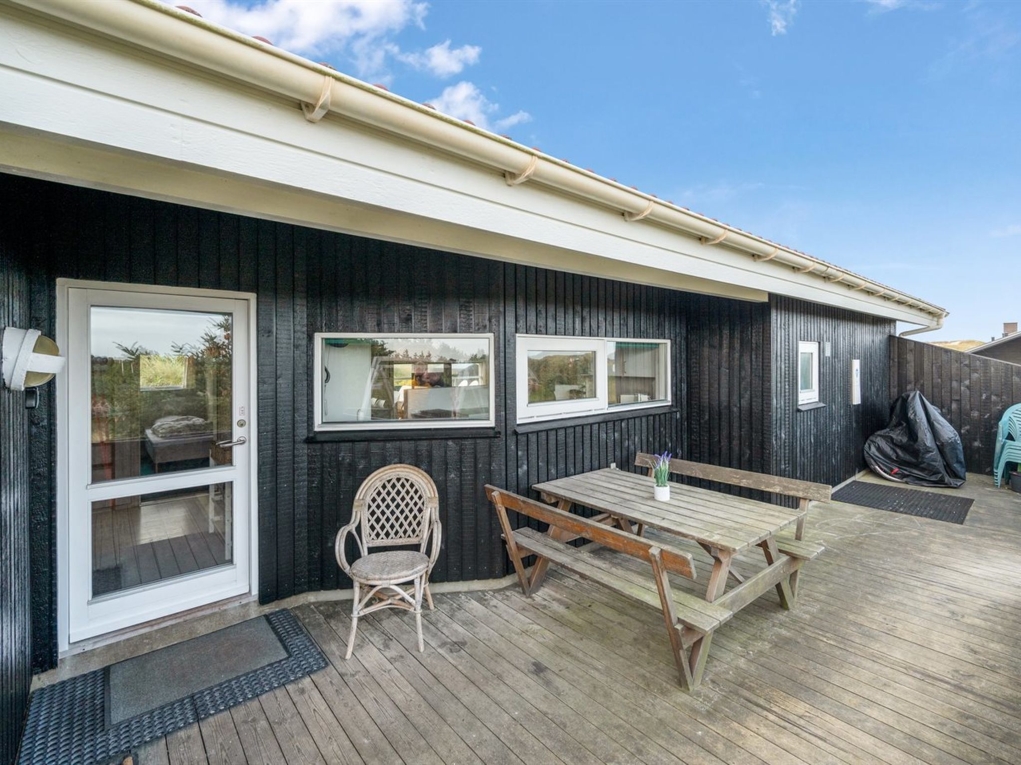 A wooden deck with a picnic table and chairs, a covered bench, and a door with glass panels.