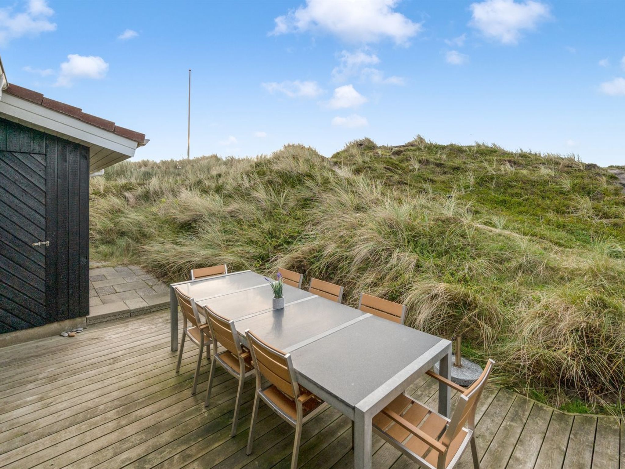 A deck with a table and chairs, overlooking a grassy dune landscape.