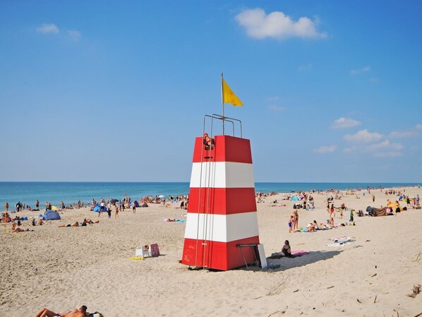 Una playa con una torre de salvavidas, arena y gente tomando el sol.