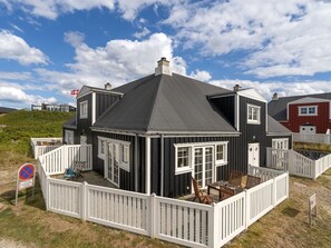 Ein zweigeschossiges Haus mit dunklem Dach, weißem Zierdekor und einem eingezäunten Patio.