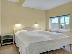 Ein Schlafzimmer mit Bett, Nachttischlampen, einem Nachttisch und einem Fenster.