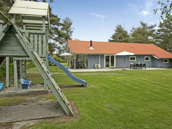 A house with a red-tiled roof, a covered patio with outdoor furniture, and a grassy yard.