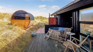 A wooden deck with a hot tub, wooden chairs, and a large wooden barrel structure.