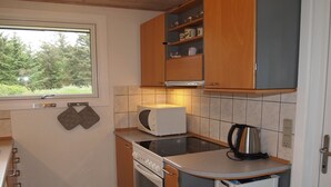 A compact kitchen with a microwave, stove, and kettle. There is a window with a view of greenery outside.