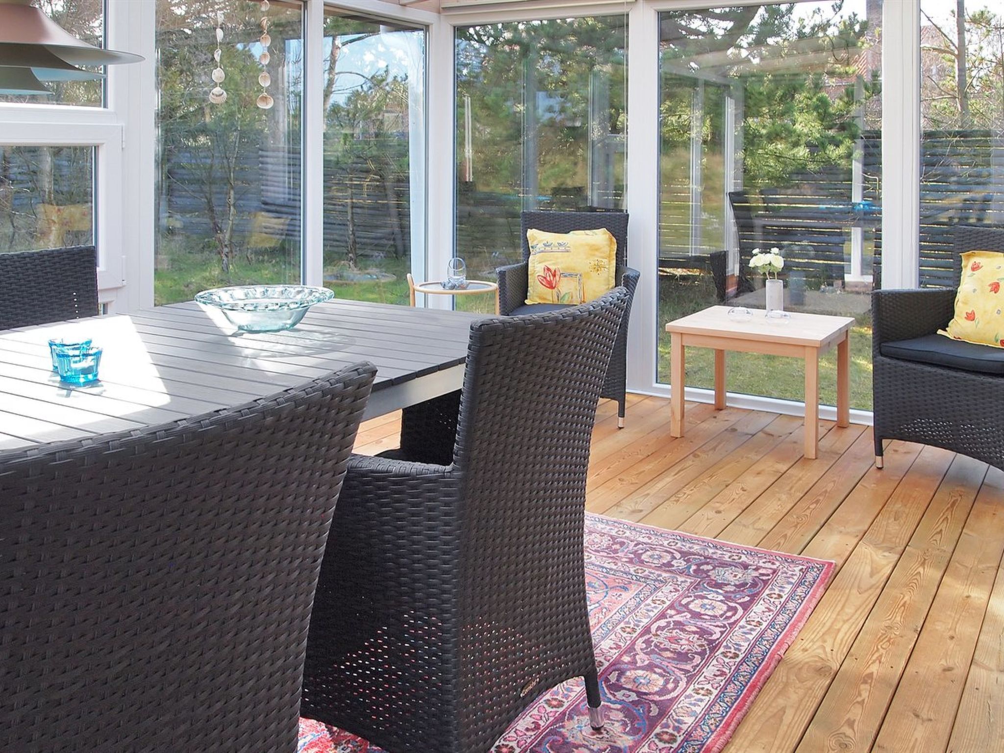 A covered patio with wicker furniture, a glass table, and a patterned rug.