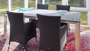 A dining area with a table and chairs, a hanging light fixture, and a view of the backyard through large windows.