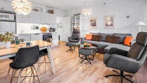 Una sala de estar moderna con un sofá gris, sillas negras, una mesa de comedor de madera y una cocina al fondo.