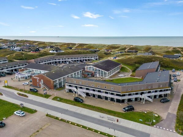 A coastal hotel with multiple buildings, parking, and a view of the sea.