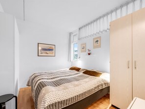 Een slaapkamer met een bed, een kledingkast, een stoel en een raam met gordijnen.