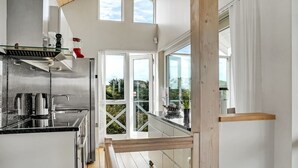 Eine moderne Küche mit großem Fenster, einer Holzterrasse und Blick ins Grüne.