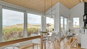 Ein modernes Interieur mit großen Fenstern, Holzböden und einem Essbereich mit weißen Stühlen.
