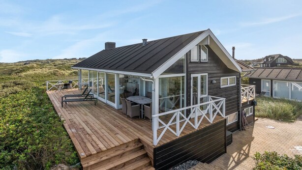 Ein modernes Strandhaus mit Holzterrasse, Glasfenstern und einem schwarzen Dach.