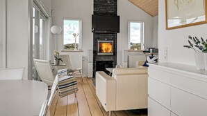 Ein modernes Wohnzimmer mit Kamin, weißen Möbeln und Blick ins Freie.